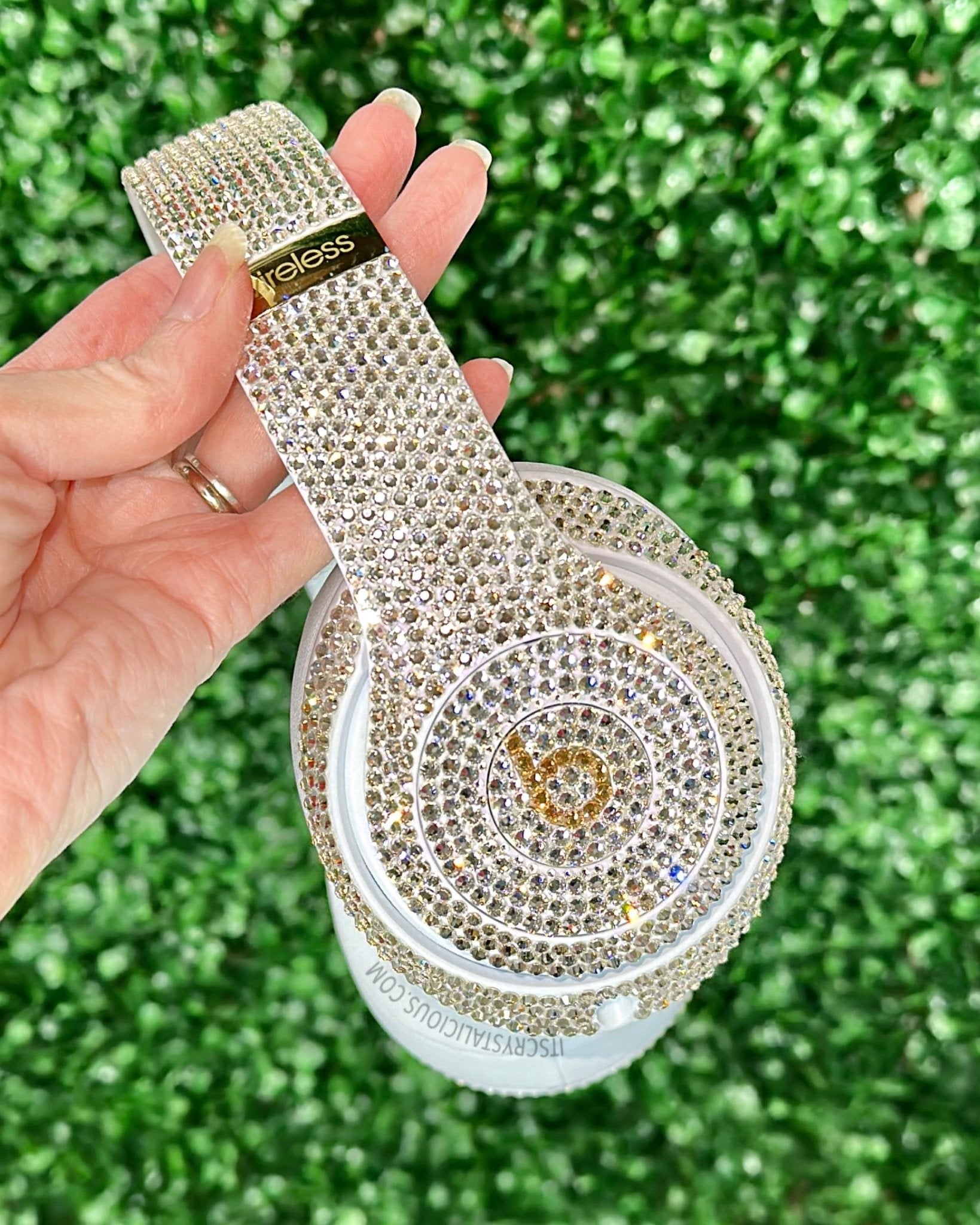 Hand holding a blinged-out electronic device against a green grass background