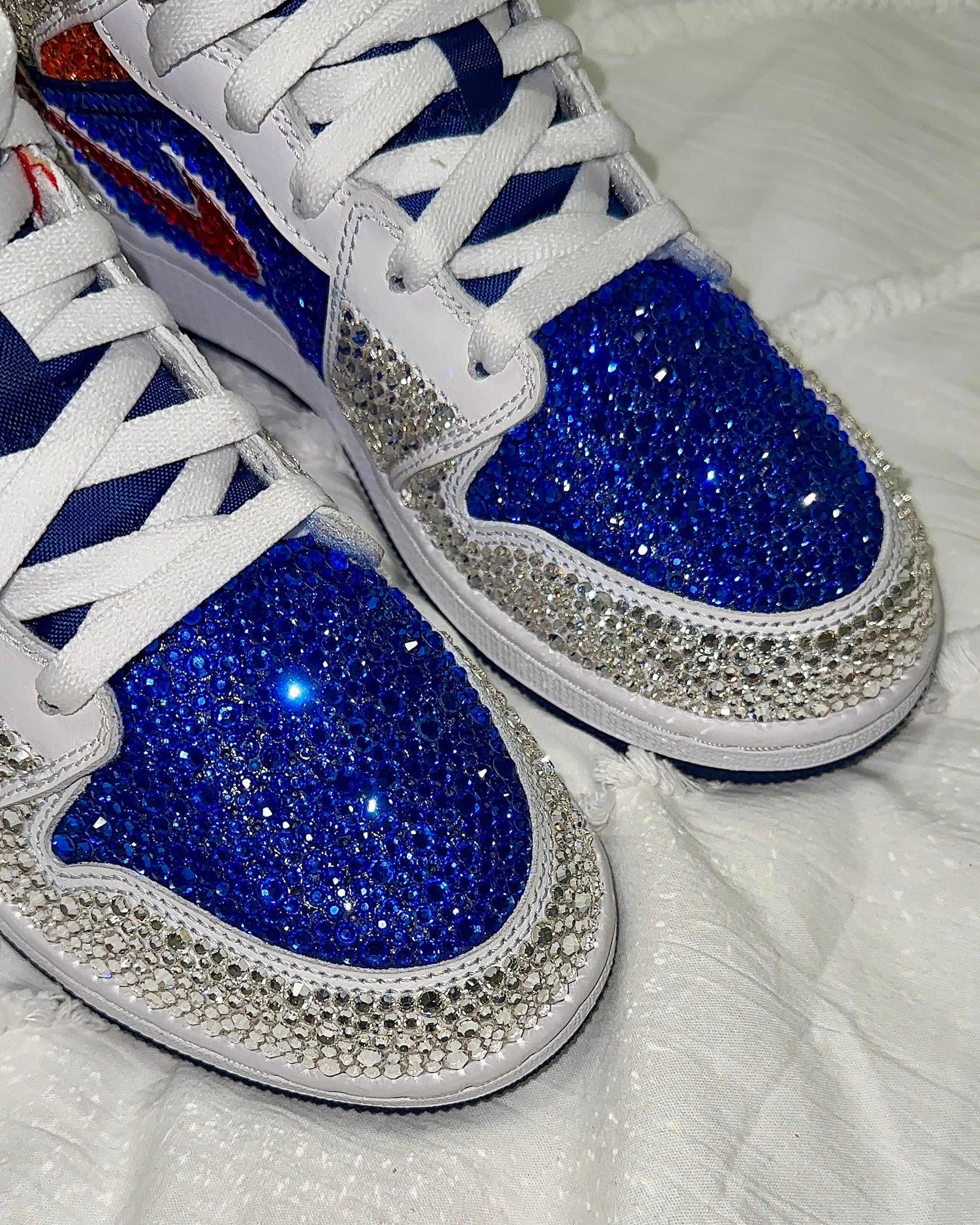 White sneakers with blue soles and silver rhinestone embellishments on a white background