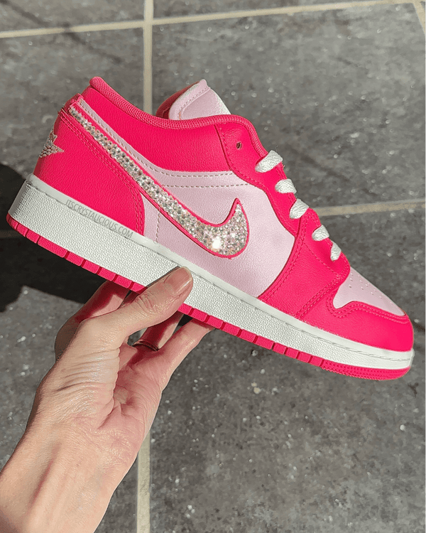Pink sneaker with a large Nike logo held by a hand on a tiled floor.