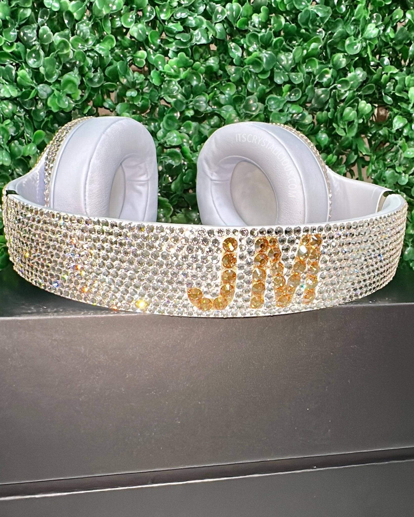 White headphones with gold 'JW' lettering on a green leafy background