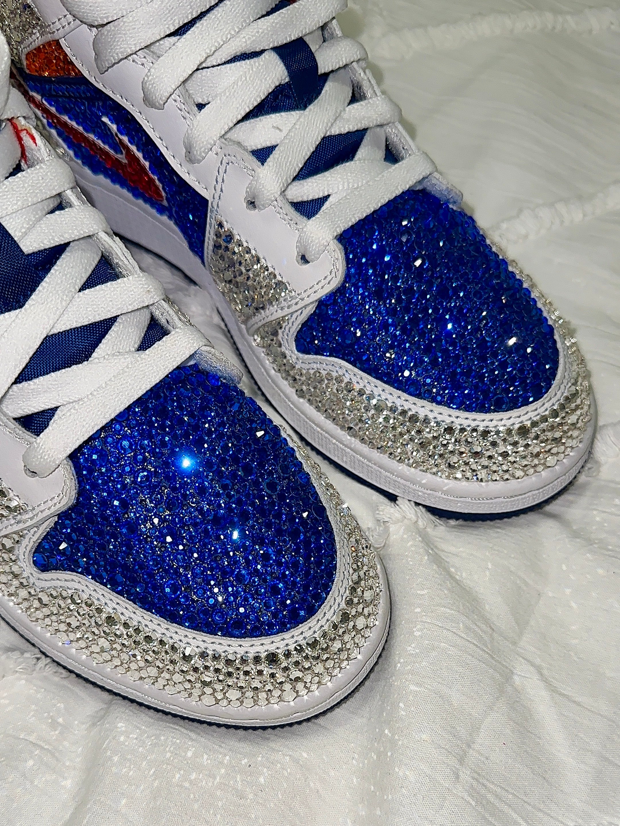 White sneakers with blue soles and silver rhinestone embellishments on a white background