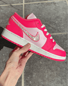 Pink sneaker with a large Nike logo held by a hand on a tiled floor.